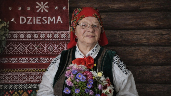 Attēlā Zenta Bērtiņa tautas tērpā ar vasaras ziedu pušķi.