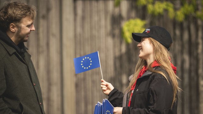 Sieviete ar Eiropas Savienības karodziņu rokās, ko sniedz vīrietim