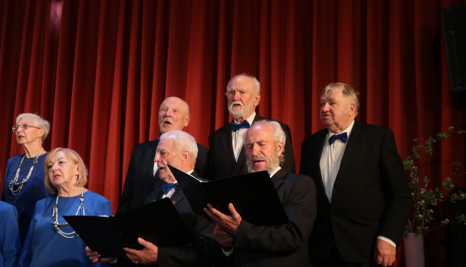 Vīri un sievas dzied, rokās turot nošu lapu mapes