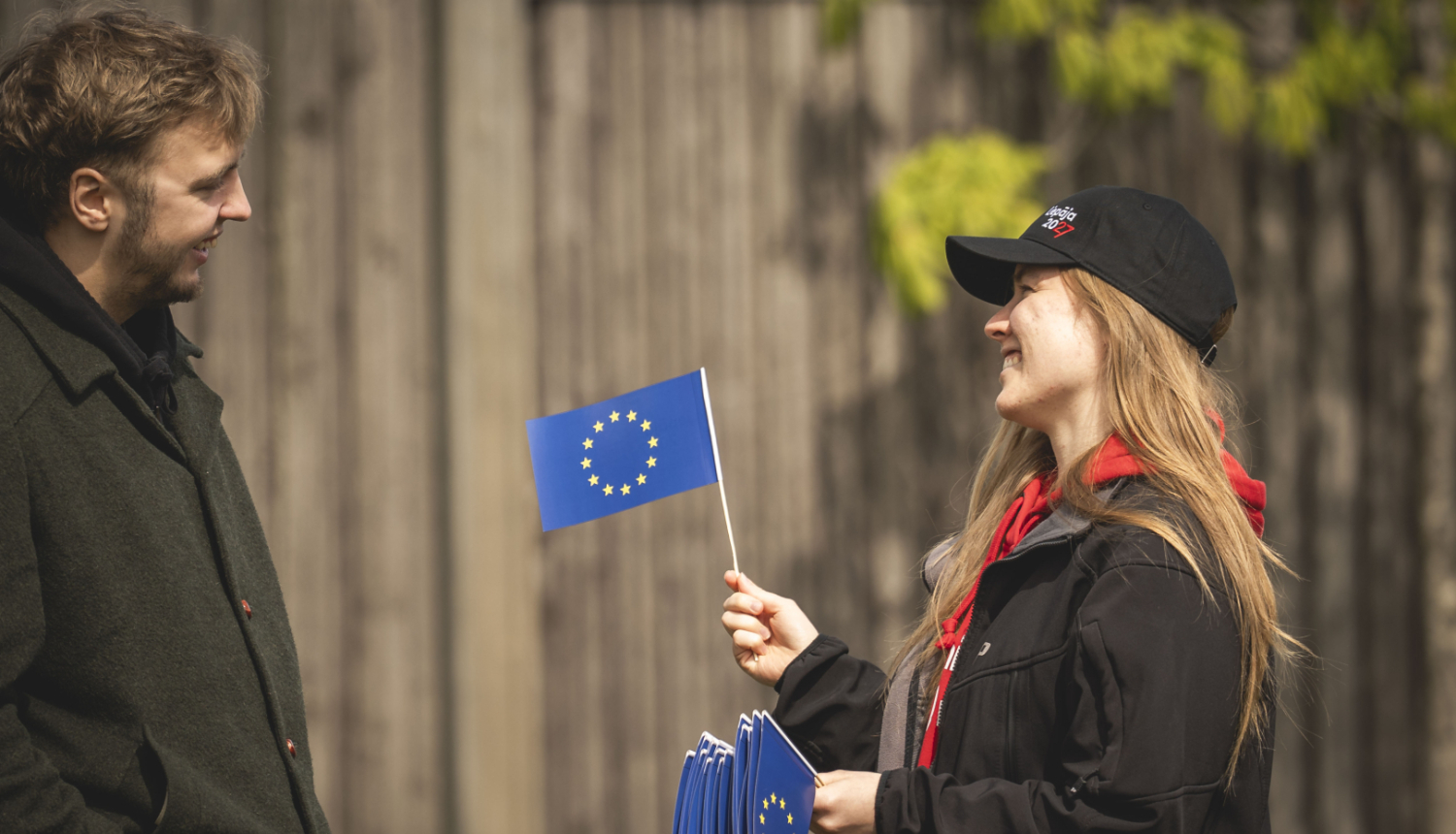 Sieviete ar Eiropas Savienības karodziņu rokās, ko sniedz vīrietim